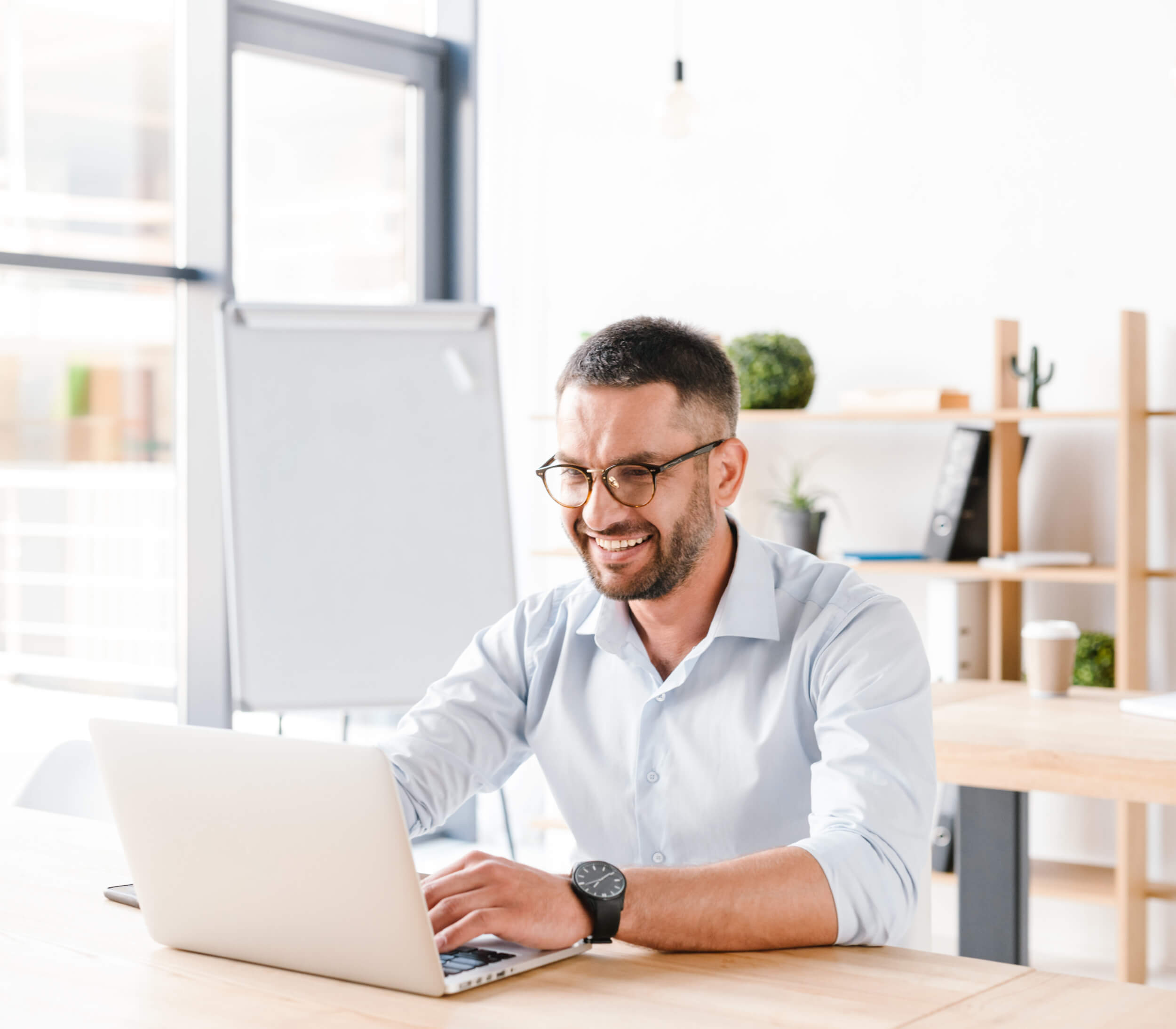 Photo of joyous office man 30s in white shirt sitting at desk, and working on laptop in business centre